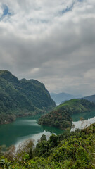 Scenic view of lush green mountains and a serene lake under a cloudy sky, ideal for nature retreats and holidays
