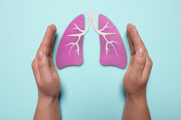 Woman holding hands near illustration of lungs on light blue background, closeup. Asthma and other...