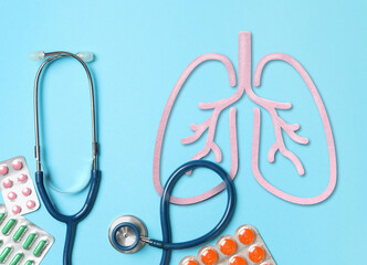 Stethoscope, drugs and illustration of lungs on light blue background, flat lay. Asthma and other...