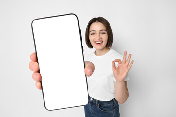 Happy woman showing mobile phone with blank screen on white background. Mockup for design