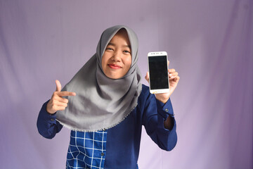 Portrait of a woman calling happily, an Indonesian Muslim woman smiling happily at the camera with a smartphone in her hand