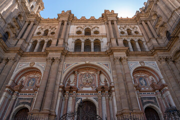 A striking view of the intricate facade of M&aacute;laga Cathedral, showcasing its grand architecture against a clear blue sky. Ideal for themes of historic landmarks, architecture, and Spanish heritage.