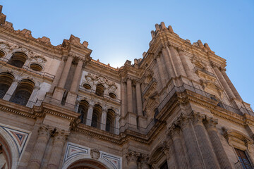 A striking view of the intricate facade of Málaga Cathedral, showcasing its grand architecture against a clear blue sky. Ideal for themes of historic landmarks, architecture, and Spanish heritage.