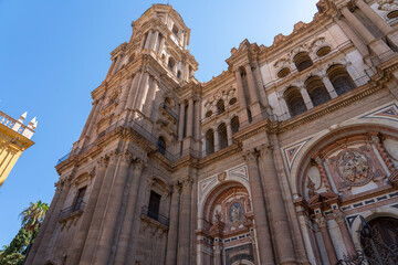 Fototapeta premium A striking view of the intricate facade of Málaga Cathedral, showcasing its grand architecture against a clear blue sky. Ideal for themes of historic landmarks, architecture, and Spanish heritage.