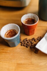 Two cups of espresso with coffee beans on a wooden table.