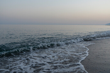 Gentle waves lap the shore at dusk on a tranquil beach in M&aacute;laga, Spain. Perfect for themes of relaxation, coastal serenity, and nature's beauty.