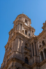A striking view of the intricate facade of Málaga Cathedral, showcasing its grand architecture against a clear blue sky. Ideal for themes of historic landmarks, architecture, and Spanish heritage.