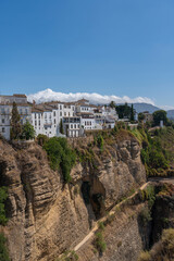 Obraz premium A stunning view of whitewashed houses perched on the edge of the Tajo Gorge in Ronda, Spain, with rugged cliffs and a clear blue sky. Perfect for themes of travel, architecture, and scenic landscapes.