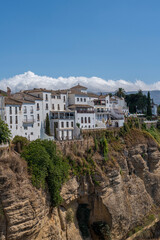 Obraz premium A stunning view of whitewashed houses perched on the edge of the Tajo Gorge in Ronda, Spain, with rugged cliffs and a clear blue sky. Perfect for themes of travel, architecture, and scenic landscapes.