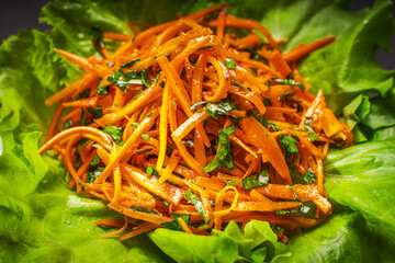 Carrot salad with parsley in Vinaigrette sauce on a gray background. Carrots cut into thin strips on lettuce leaves.