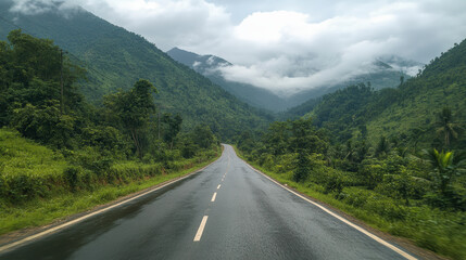 Fototapeta premium A wet, winding road cuts through lush, verdant hills shrouded in mist, creating a serene, picturesque scene of natural beauty and tranquility.