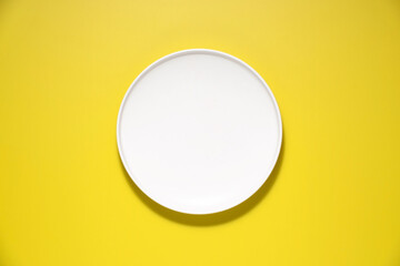 Top down view of a white plate isolated on yellow background with copy space