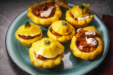 Pumpkins stuffed with roasted turkey and cheese baked on a turquoise plate on a gray background