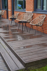 Close up of wicker chairs and sofa with red brick building on the back with glass windows. After the rain. Wooden steps to veranda. Summer day. Tallinn, Estonia, Europe. July 2024