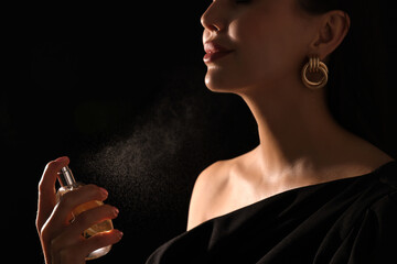 Woman spraying perfume on black background, closeup