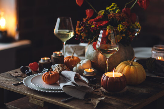 Fall composition. Orange pumpkins, flowers and candles on wooden table. Family elegant Thanksgiving or halloween dinner. Cozy autumn concept, simple handmade decoration, countryside style, wine