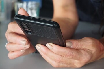 Frau hält Handy in ihren Händen abgestützt auf grauer Tischplatte in Raum