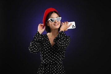 Stylish woman listening to voice message via smartphone on dark background