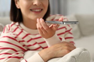 Woman recording voice message via smartphone at home, closeup