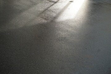Silhouette von Fenster mit Sonnenlicht auf nassem grauen Asphaltboden bei Sonne und Regen am Abend...