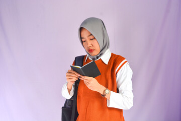 Portrait of a muslim schoolgirl carrying books in her hands and wearing a black backpack on an isolated background