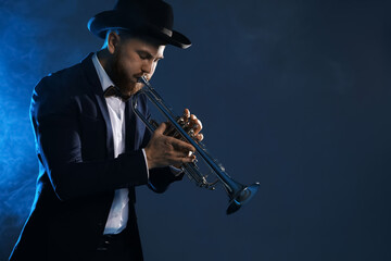 Fototapeta premium Professional musician playing trumpet on dark background in blue lights and smoke. Space for text