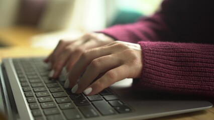 Close-up of a young girl's hands typing on a laptop in a cafe.