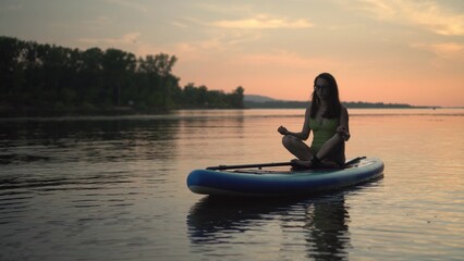 A Woman Meditating Peacefully on a Paddleboard While Enjoying a Beautiful Sunset Moment