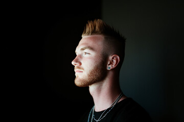 Obraz premium Closeup portrait of a Caucasian man with a short, spiked hairstyle and a light stubble beard, black background