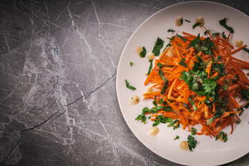 Carrot and parsley salad with Vinaigrette sauce on a white plate on a gray background. A place to copy the space.