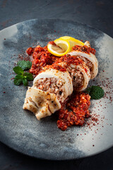 Fried calamari tubes stuffed with rice in salsiccia mince tomato sauce served as close-up on a design plate with copy space