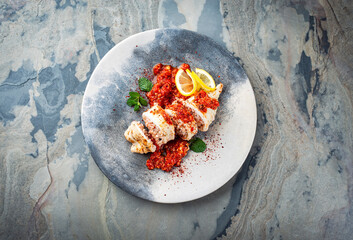 Fried calamari tubes stuffed with rice in salsiccia mince tomato sauce served as top view on a design plate with copy space