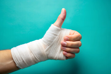 Bandaged hand and thumb up gesture on green background close up