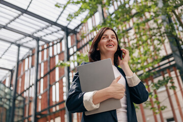 A successful businesswoman in a modern glass building holding a laptop while on a phone call