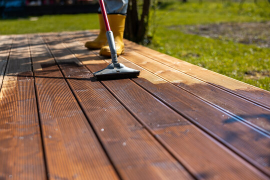 Person applying stain to a wooden deck in a backyard, focusing on maintenance and care of outdoor spaces