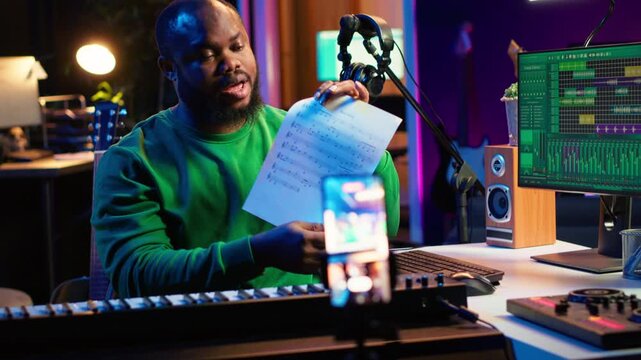 Talented composer explaining musical sheet notes during online master class recorded with smartphone in home studio. Artist musician teaching people how to read and sing accords on piano. Camera A.