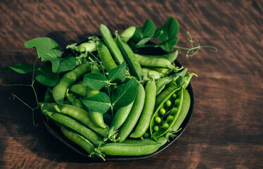 Green peas in a bowl on a wooden background closeup. Green pea pods and leaves. Healthy food.