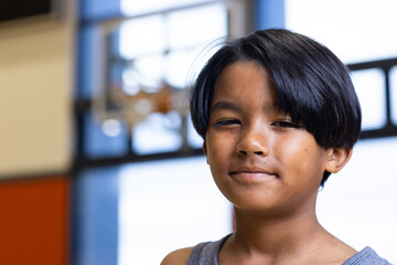 Smiling boy in school gymnasium with basketball hoop in background