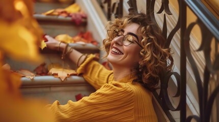 Obraz premium A young woman with curly hair smiles brightly as she sits on a staircase covered in autumn leaves.