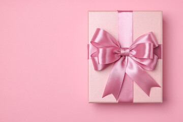 Beautiful gift box with color bow on pink background, top view. Space for text