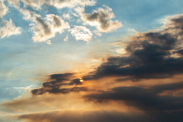 A bright blue background with fluffy white clouds in the sky. There are dark black clouds in the lower section with a bright orange sun behind the cloudy atmosphere. The stormy weather is moving.