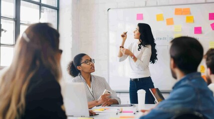 A confident businesswoman pointing at a whiteboard during a strategy meeting, with team members collaborating in the background. Ideal for themes of leadership, teamwork, and business strategy.