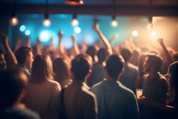Blurred image of a crowd of people in a dimly lit venue, with some raising their hands.