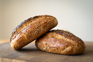 Two loaves of sourdough bread, freshly baked and still warm, are stacked on a wooden surface. The loaves are covered in seeds sesame and sunflower, adding a rustic and flavorful touch.