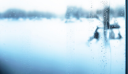 Blurred winter landscape seen through a window with condensation and water droplets

