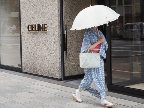TOKYO, JAPAN - August 9, 2024: Street in Tokyo's Ginza area with a yukata-clad person holding a parasol and a Celine store on a hot day.
