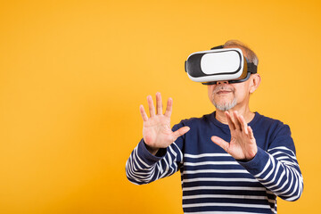Portrait Asian smiling old man touching at something in a virtual reality glasses headset studio shot isolated yellow background, Excited happy senior man pensioner using VR play simulation game
