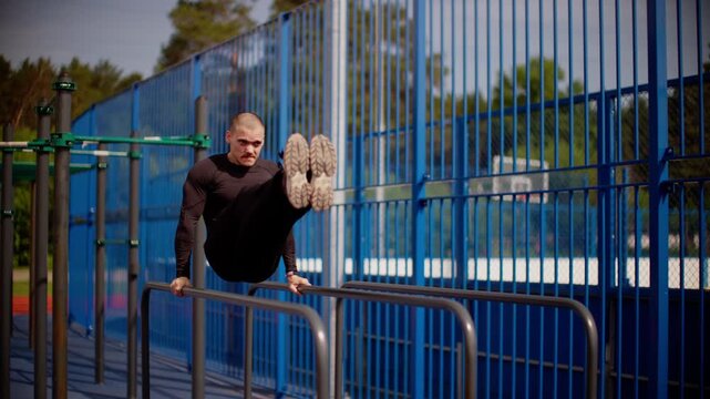 Sculpted man demonstrates dip exercises on parallel bars in slow motion