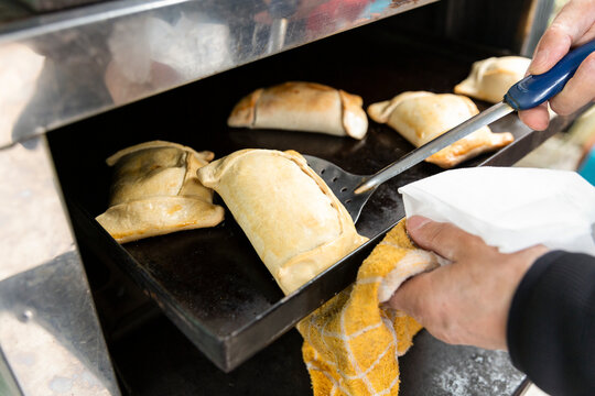man putting a Chilean empanada into an oven. Empanada is a Chilean dough filled with meat, onion, olives and egg