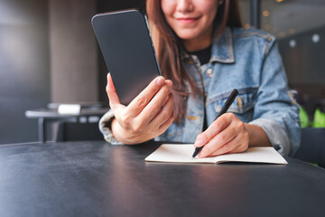 Closeup image of a woman writing on a notebook while using smart phone